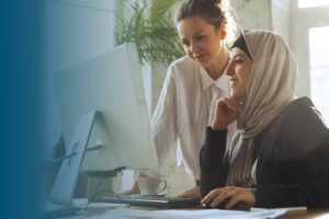 beautiful arabian woman in hijab working at computer observed by female colleague standing behind