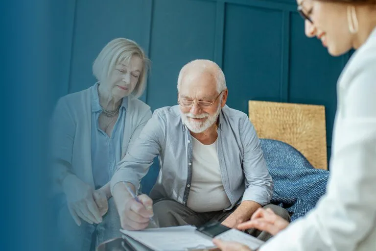 senior couple signing papework sitting with consultant in office bl